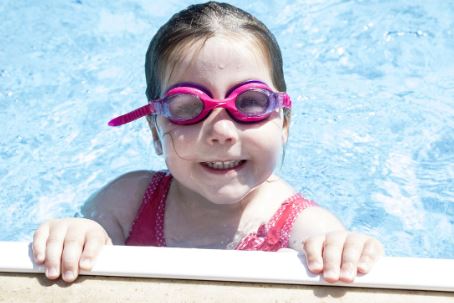 Young girl with goggles smiling at the camera and holding onto the side in a clean pool in Benton Arkansas