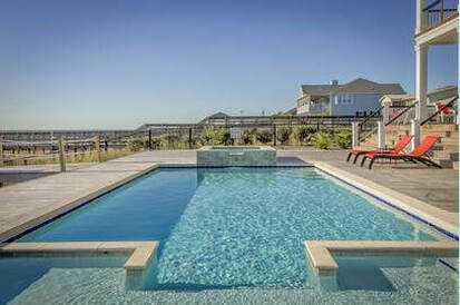 Beautiful picture of shimmering swimming pool and hot tub with a tiled deck with red chairs