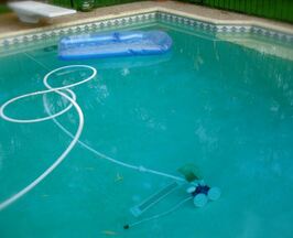 Picture of a pool vacuum Polaris running on the bottom of a somewhat dirty pool with the hose floating across the top of the water